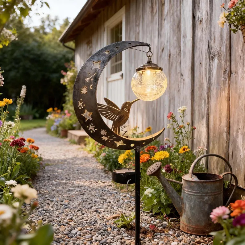 Hummingbird moon garden stake light beside flowers and pathway